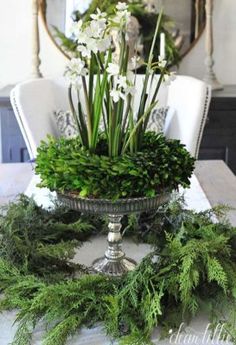 an arrangement of flowers and greenery in a bowl on top of a dining room table