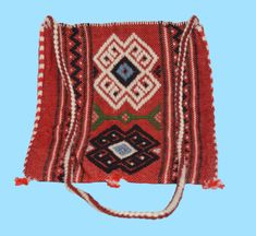 an old red and black bag with tassels on the bottom, sitting against a blue background