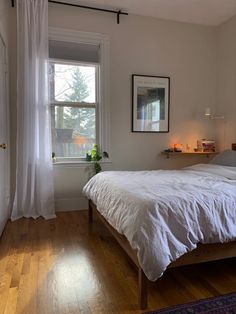 a white bed sitting next to a window on top of a hard wood floored floor