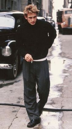 a man standing next to a fire hydrant on a wet street with an old car in the background