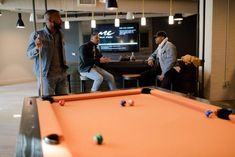 three men are playing pool in an office