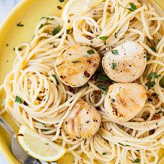 a yellow bowl filled with pasta and scallops on top of a white table