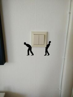 two black silhouettes are on the wall next to a white light switch and toilet