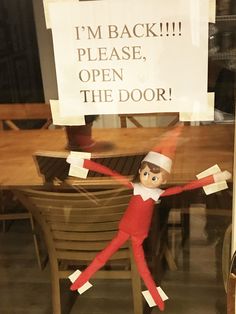 an elf is sitting in front of a sign that says i'm back please, open the door