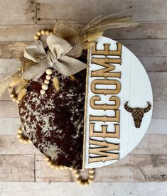 a brown and white cake with the word welcome home on it's side next to a beaded bow