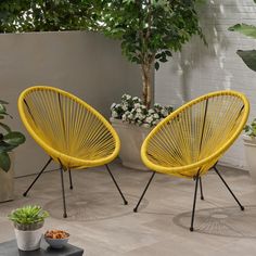 two yellow chairs sitting next to each other on top of a cement floor near potted plants