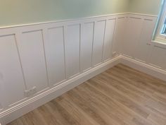 empty room with wood flooring and white paneling on the walls, along with a window