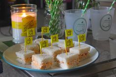 several small sandwiches on a plate with candles and cups in the backgroung