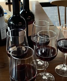 three wine glasses are sitting on a table next to two bottles and one glass is empty