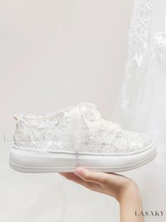 a person holding a white wedding shoe in front of a lace covered veil with the word lazay written on it