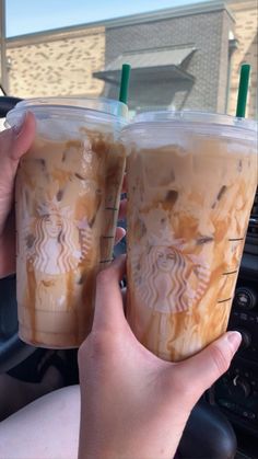 two people are holding up starbucks drinks in their hands while they drive down the street