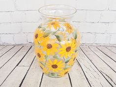 a glass vase with sunflowers painted on the outside and inside, sitting on a wooden floor