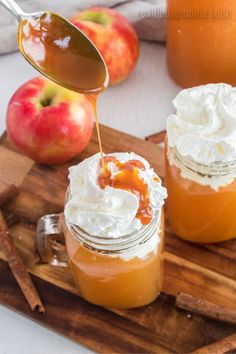 two jars filled with apple cider and whipped cream on top of a wooden cutting board