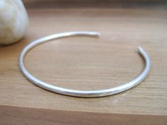 Heavy gauge sterling silver wire has been forged and formed into this lightweight, minimalist bangle bracelet. It has a glimmering texture created with a hammer, which also gives it strength and shape retention. The ends have been slightly rounded and flattened for comfort. It's a great stand alone piece, or layer it with your other favorite bracelets.The bracelet is 6 inches around and the inside of it measures 2-1/4 inches and the opening is about 1 inch. It is about 3 mm wide. It is modeled o Minimalist Jewelry Silver, Minimalist Bangle, Hammered Cuff Bracelet, Bracelet Layering, Fancy Casual, Hammered Bracelet, Open Bangle Bracelet, Silver Strand, The Bangles