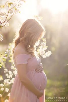 a pregnant woman in a pink dress standing next to a tree with white flowers on it