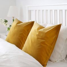 two yellow pillows sitting on top of a white bed