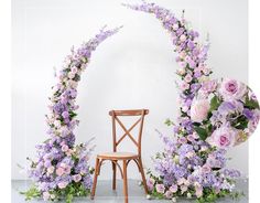 a wooden chair sitting in front of a purple flower arch with pink and white flowers