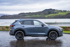 a blue mazda cx - 5 parked in front of a body of water on a rainy day