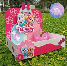 a pink and blue box with paw patrol characters on it in the middle of some green grass