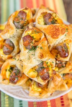 a white plate topped with sausage and cheese pastries on top of a colorful table cloth