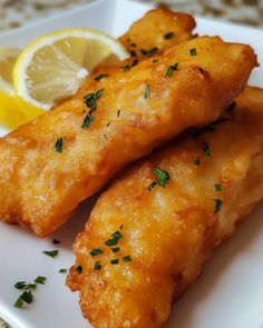 two pieces of fried fish on a plate with lemon wedges and parmesan cheese