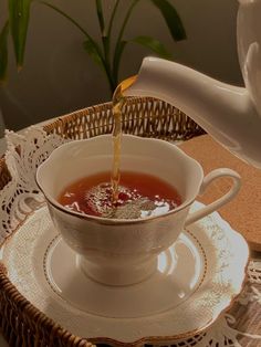 tea being poured into a white cup on top of a saucer and lace doily