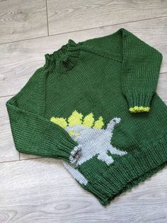 a green sweater with yellow and white dinosaur on it sitting on top of a wooden floor