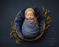 a newborn baby wrapped in a blue blanket and wearing a yellow headband is posed on a wooden bowl