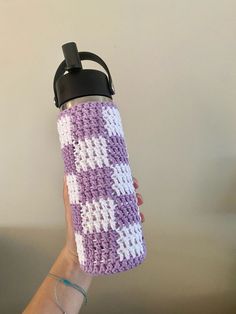 a hand holding a purple and white crocheted water bottle cover