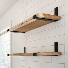 two wooden shelves mounted to the side of a white brick wall with black metal brackets