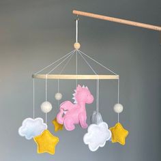 a pink and yellow baby mobile hanging from a wooden rod with stars, clouds, and a unicorn on it