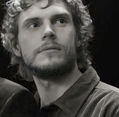 a black and white photo of a man with curly hair looking to the side, in front of a dark background