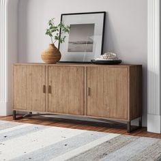 a wooden cabinet with a plant on top in front of a white and gray wall