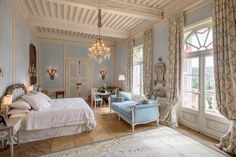 a large bedroom with blue walls and white bedding, chandelier, windows, and furniture