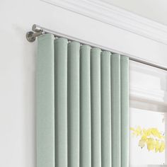 a green curtain hanging on the side of a white wall next to a window with yellow flowers