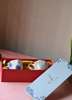 an open box with two decorative items inside it on a table next to a potted plant