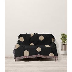 a black and white polka dot couch with fringes on the bottom, next to a potted plant