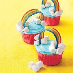 three cupcakes with blue icing and rainbow decorations