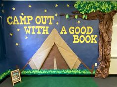 a camp out with a good book sign in front of a wall decorated with trees and grass