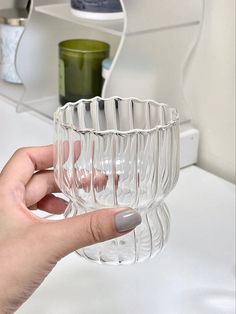 a person holding a clear glass cup in front of a mirror on a bathroom counter