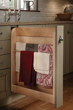 an open cabinet in the middle of a kitchen with towels hanging from it's sides