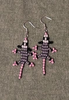 two pink and black beads are hanging from silver earwires on a gray surface