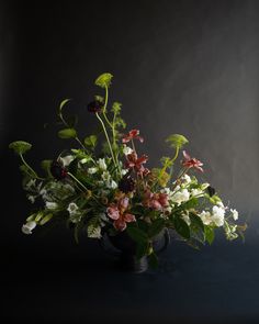 a vase filled with lots of flowers on top of a blue tablecloth next to a black wall