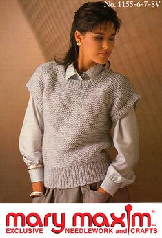 a woman wearing a white sweater and gray pants with her hands on her hips, standing in front of a wall