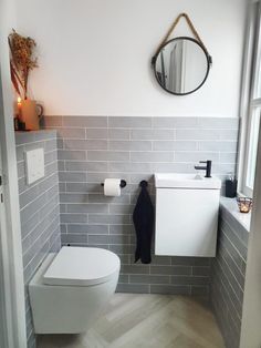 a white toilet sitting next to a sink in a bathroom under a round mirror on the wall