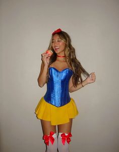 a woman in a blue and yellow corset holding an apple while standing next to a wall