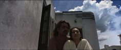 a man and woman sitting next to each other in front of a building with shutters