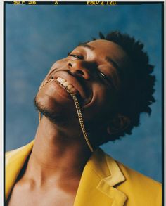 a man with a gold chain around his neck and eyes closed wearing a yellow shirt