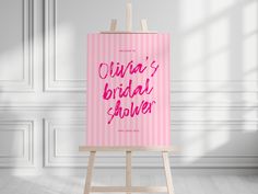 an easel with a pink poster on it in front of a white wall that says oura's bridal shower