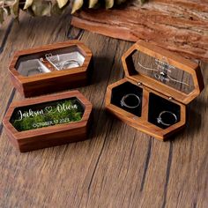 two wooden boxes with wedding rings inside on top of a wood table next to other jewelry